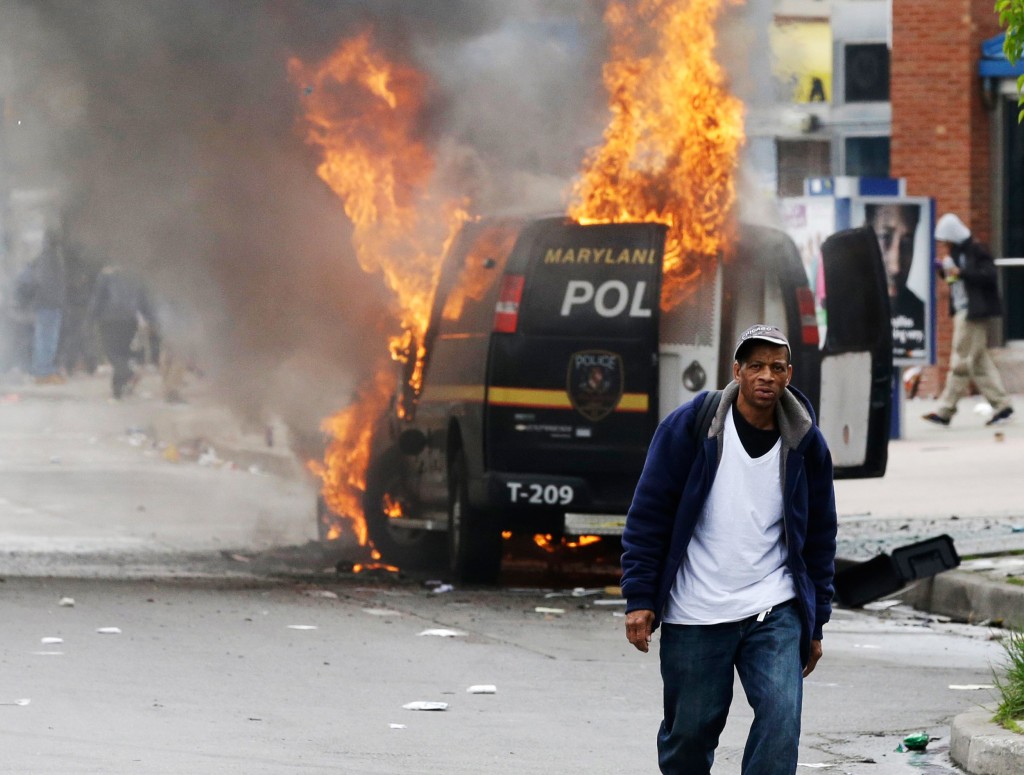 A man walks past a burning police vehicle, Monday, April 27, 2015, during unrest following the funeral of Freddie Gray in Baltimore. Gray died from spinal injuries about a week after he was arrested and transported in a Baltimore Police Department van. (AP Photo/Patrick Semansky)